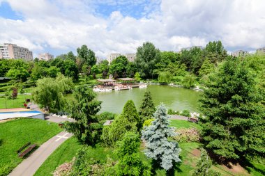 Romanya 'nın Bükreş kentindeki Moghioros Parkı olarak da bilinen Drumul Taberei Parkı' nda (Parcul Drumul Taberei), bulutlu bir yaz gününde göl ve canlı yeşil ağaçlarla çevrili manzara