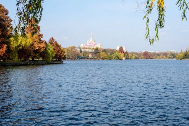 Bucharest, Romania, 6 November 2021: Landscape with white boat on Herastrau lake and large green trees in King Michael I Park (Herastrau) in Bucharest, Romania, in a sunny autumn day