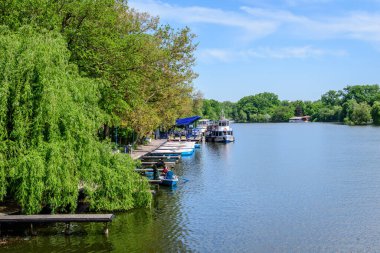 Bükreş, Romanya - 15 Mayıs 2021: Romanya 'nın başkenti Bükreş' te güneşli bir bahar gününde Herastrau Gölü 'ndeki beyaz tekne ve Kral I. Michael Park' taki (Herastrau) büyük yeşil ağaçlarla manzara