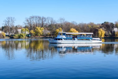 Bucharest, Romania, 21 November 2021: Landscape with white boat on Herastrau lake and large green trees in King Michael I Park (Herastrau) in Bucharest, Romania, in a sunny autumn day