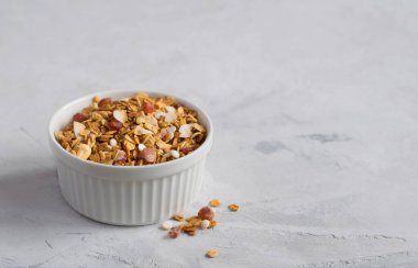 Tahıl gevreğiyle beyaz bir kase, ışık masasında eziliyor. Sağlıklı bir kahvaltı için fındıklı ve kuru meyveli granola. Uzayı kopyala Seçici odak.