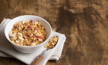 Kahverengi bir kırsal masada beyaz bir kase müsli. Sağlıklı bir kahvaltı için fındıklı ve kuru meyveli granola. Boşluğu kopyala. Seçici odak.