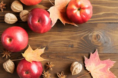 Ahşap bir tahtanın üzerindeki renkli yapraklar, elmalar, fındıklar ve baharatların sonbahar arkaplanı. Sonbahar arkaplanı. Düz konum, üst görünüm, kopyalama alanı.