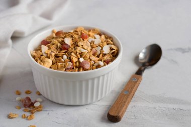 Açık beton bir masada beyaz bir kase ev yapımı granola. Sağlıklı bir kahvaltı için fındıklı ve kuru meyveli granola. Yakın plan. Seçici odak.