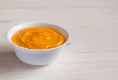 Pumpkin puree soup in a white bowl on a light wooden background. The concept of thanksgiving. Copy space.