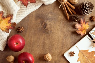 Sonbahar arka planında doğal çam kozalakları, kurumuş yapraklar, elmalar ve baharatlar kahverengi ahşap bir tahtanın üzerinde sıcak örülmüş bir battaniye. Uzayı kopyala Konforlu düz yerleşim.