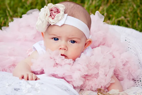 Cute newborn girl in pink skirt gnaws fingers — Stock Photo, Image