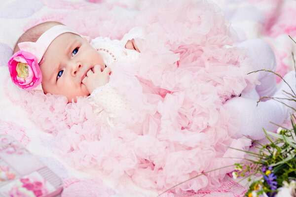 Cute newborn girl in pink skirt gnaws fingers