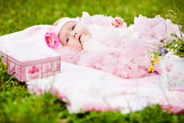 Cute newborn girl in pink skirt gnaws fingers — Stock Photo, Image