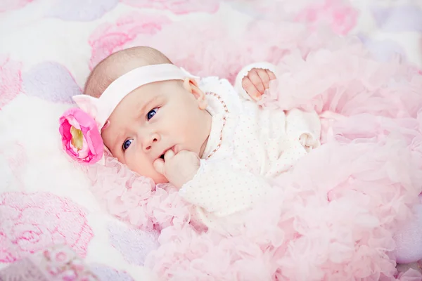 Cute newborn girl in pink skirt gnaws fingers — Stock Photo, Image