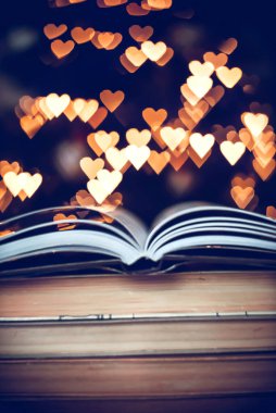 Geçmişe dönük bir yığın kitap ve arka planda Bokeh Heart ışıkları. Sevgililer Günü konsepti