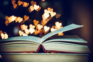 Geçmişe dönük bir yığın kitap ve arka planda Bokeh Heart ışıkları. Sevgililer Günü konsepti