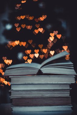 Geçmişe dönük bir yığın kitap ve arka planda Bokeh Heart ışıkları. Sevgililer Günü konsepti