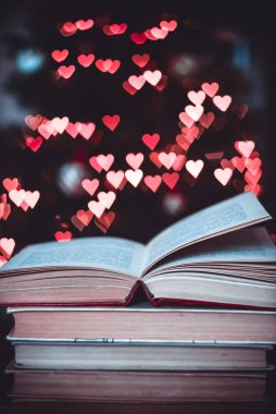 Geçmişe dönük bir yığın kitap ve arka planda Bokeh Heart ışıkları. Sevgililer Günü konsepti