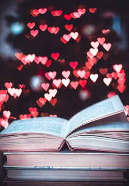 Geçmişe dönük bir yığın kitap ve arka planda Bokeh Heart ışıkları. Sevgililer Günü konsepti