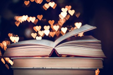 Geçmişe dönük bir yığın kitap ve arka planda Bokeh Heart ışıkları. Sevgililer Günü konsepti