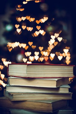Geçmişe dönük bir yığın kitap ve arka planda Bokeh Heart ışıkları. Sevgililer Günü konsepti
