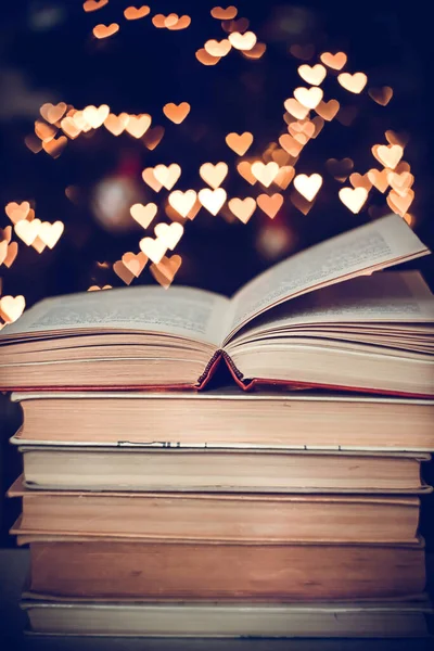 Geçmişe dönük bir yığın kitap ve arka planda Bokeh Heart ışıkları. Sevgililer Günü konsepti