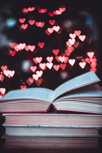 Geçmişe dönük bir yığın kitap ve arka planda Bokeh Heart ışıkları. Sevgililer Günü konsepti