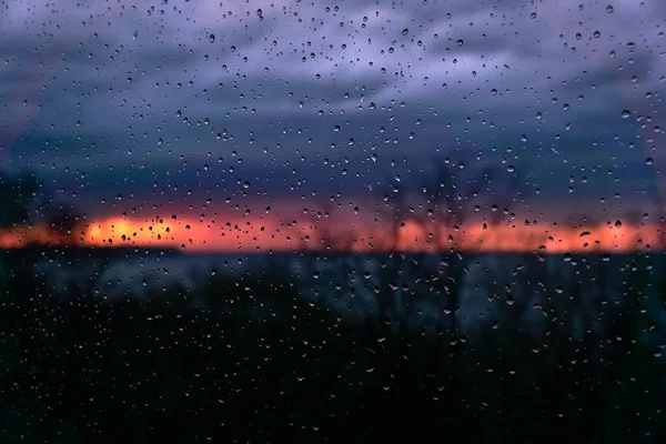 Gocce di pioggia sul vetro, sullo sfondo di un tramonto cremisi, una leggera sfocatura — Foto Stock