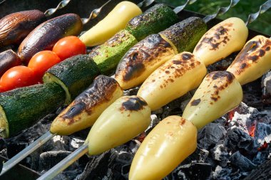 Cooking fresh vegetables on the grill, barbecue. Eggplants, peppers, tomatoes on skewers on the grill.