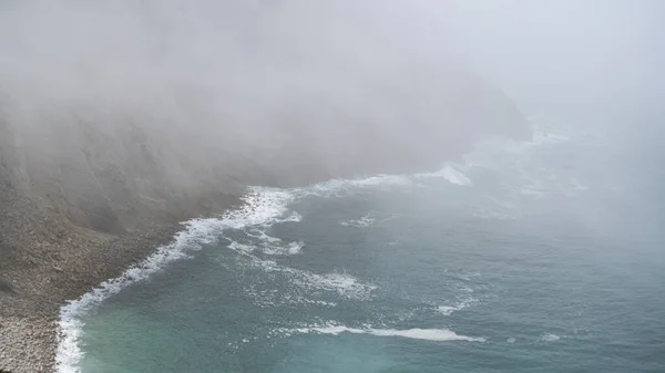 海上的雾气。雾气笼罩在岩石峭壁附近的水面上.海洋悬崖上的神秘雾. — 图库照片