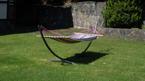 Gekleurde hangmat in de achtertuin. Stof hangmat op een metalen staanders in de tuin. Gestreepte stof hangmat met standaard — Stockfoto