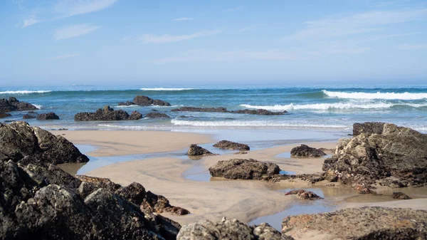 Kumsaldaki küçük uçurumlar. Portekiz kayalıkları ve dalgaları. Kumlu sahil şeridinde büyük taşlar. Alentejo, Portekiz