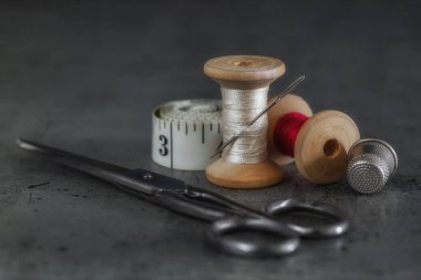 Dikiş işi için çeşitli aksesuarlar. Bir takım dikiş aletleri, iplik makaraları, kumaşlar, makas ve eski bir yüzeyde yüksük. Retro biçimi