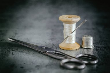 Ahşap bir makarada çok renkli iplikler, eski bir yüzeye makas yüksüğü ve terzi bandı ile dikiş iğnesi. İplik arkaplanı dikiliyor. Retro tarzı. Seçici odak