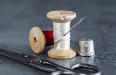 Dikiş işi için çeşitli aksesuarlar. Bir takım dikiş aletleri, iplik makaraları, kumaşlar, makas ve eski bir yüzeyde yüksük. Retro styl