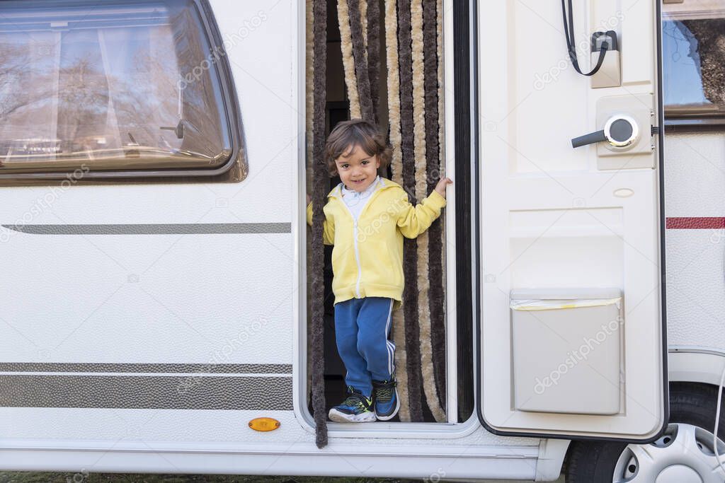 Curly haired boy at the door of his motorhome on a sunny morning.