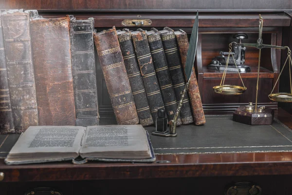 Oude ganzenveer, boeken en vintage inktpotje op houten bureau in het oude kantoor tegen de achtergrond van de boekenkast en de stralen van licht. Conceptuele achtergrond op de geschiedenis, onderwijs, literatuur onderwerpen. — Stockfoto