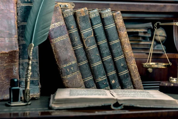 Oude ganzenveer, boeken en vintage inktpotje op houten bureau in het oude kantoor tegen de achtergrond van de boekenkast en de stralen van licht. Conceptuele achtergrond op de geschiedenis, onderwijs, literatuur onderwerpen. — Stockfoto