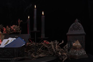 Tarot kartı doğa gösterisinde sergileniyor. Kurutulmuş bitkilerle, mavi çiçeklerle, beyaz mumlarla çevrili koyu ahşap bir masada el yapımı tarot kartları. Mavi kartlar.