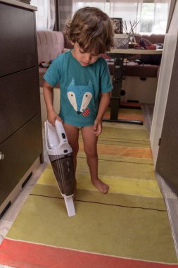 Cute and diligent baby cleans the caravan with a vacuum cleaner