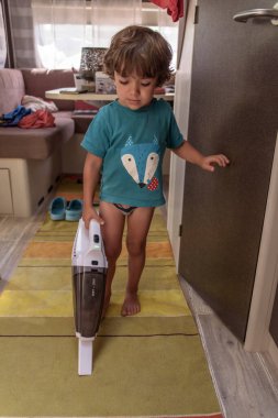 A sweet little boy vacuums the caravan while on vacation. A cute boy is cleaning the caravan