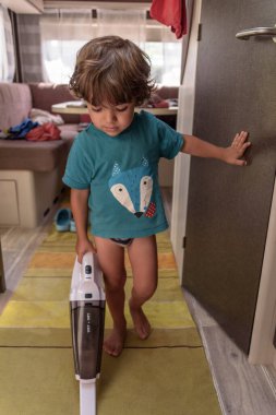 Cute and diligent baby cleans the caravan with a vacuum cleaner