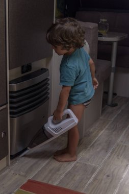 A sweet little boy vacuums the caravan while on vacation. A cute boy is cleaning the caravan