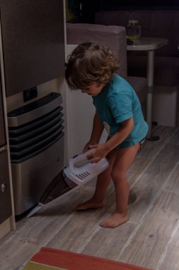 A sweet little boy vacuums the caravan while on vacation. A cute boy is cleaning the caravan