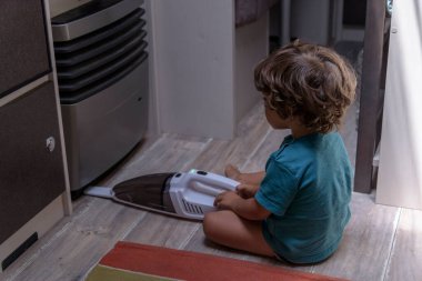 A sweet little boy vacuums the caravan while on vacation. A cute boy is cleaning the caravan