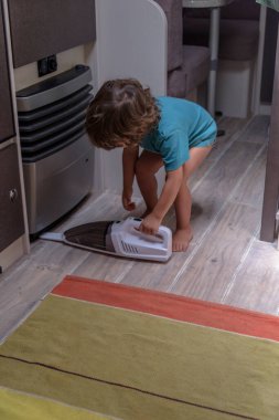 Cute and diligent baby cleans the caravan with a vacuum cleaner