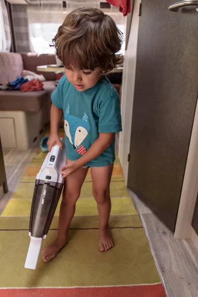 A sweet little boy vacuums the caravan while on vacation. A cute boy is cleaning the caravan