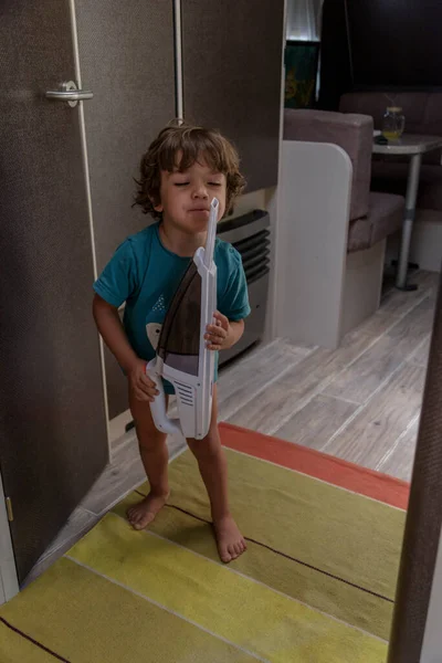 Cute and diligent baby cleans the caravan with a vacuum cleaner