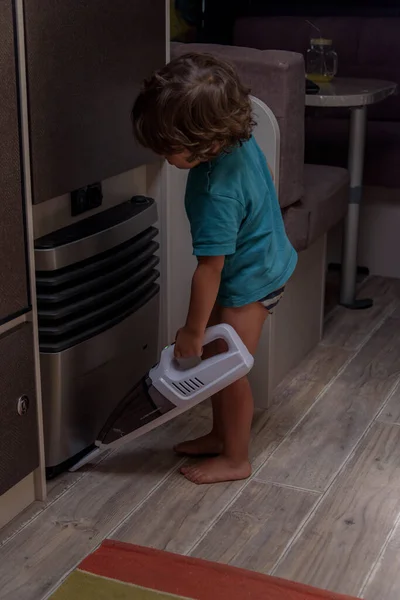 Cute and diligent baby cleans the caravan with a vacuum cleaner