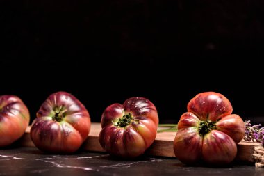 Tiger tomato on a cutting board with basil leaves on wooden background. Fresh tomato wased for cooking. Tomato with droplets of water