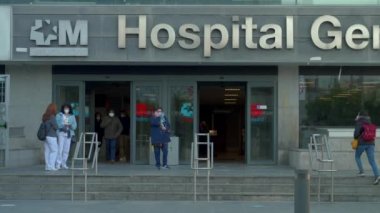 La Paz Hastanesi 'nin Madrid' deki ana girişinin orta boy fotoğrafı. Yüzü maskeli hastalar covid-19 salgını sırasında binaya girip çıkıyorlar.