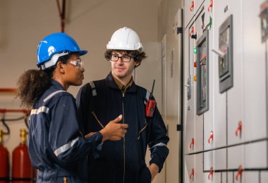 Professional engineer team man and women working at warehouse factory. Two Worker wearing safety uniform and Hard Hat checking at electrical cabinet control.