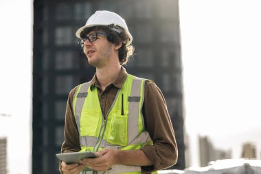 Professional engineer man working checking and maintenance pipeline construction top of the building. Worker in safety uniform using tablet at pipeline construction system