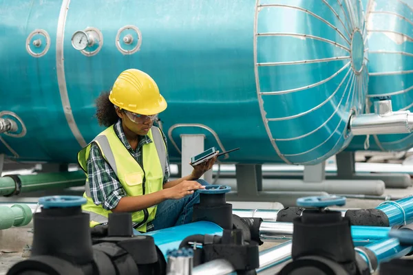 Professional engineer black women working checking and maintenance pipeline construction top of the building. Worker in safety uniform using tablet at pipeline construction system